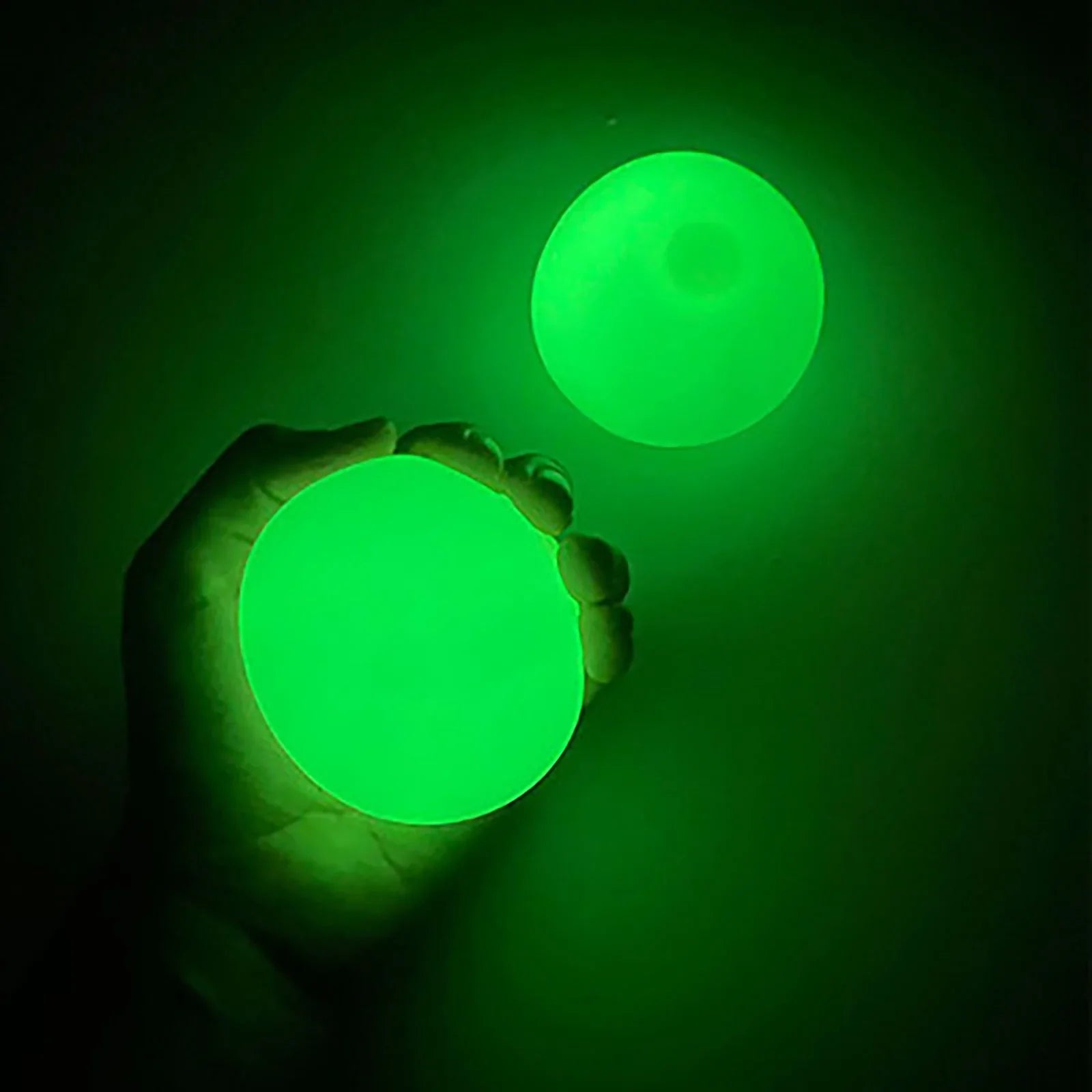 Beckett Sticky Glow Balls in various sizes glowing in the dark on a dark background, perfect for sensory play and entertainment.